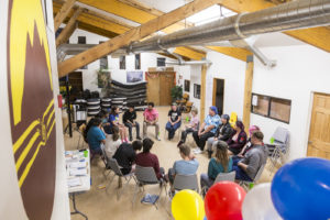 18 people sitting in a circle inside a well-lit building with high ceilings.